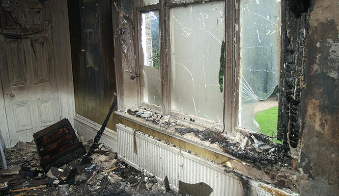 Interior of a fire-damaged room with shattered windows, charred walls and debris scattered on the floor