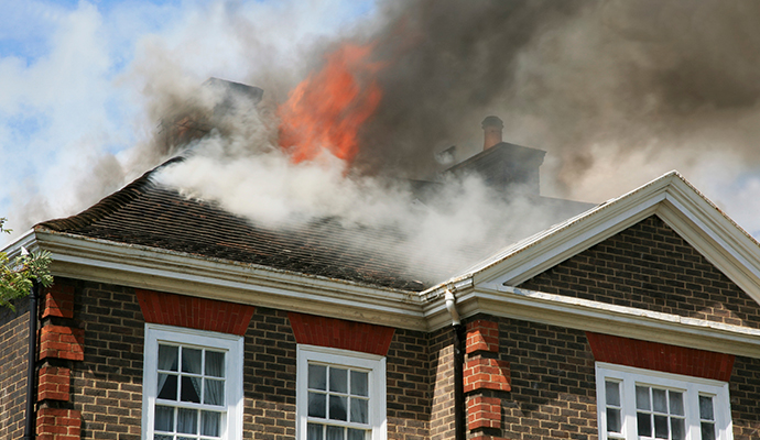 Fire damaged house with dark smoke billowing from the roof