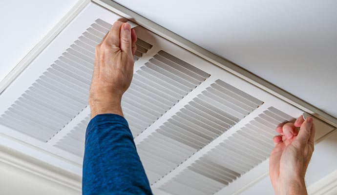 Person removing or adjusting a white air vent from a white ceiling for maintenance or cleaning