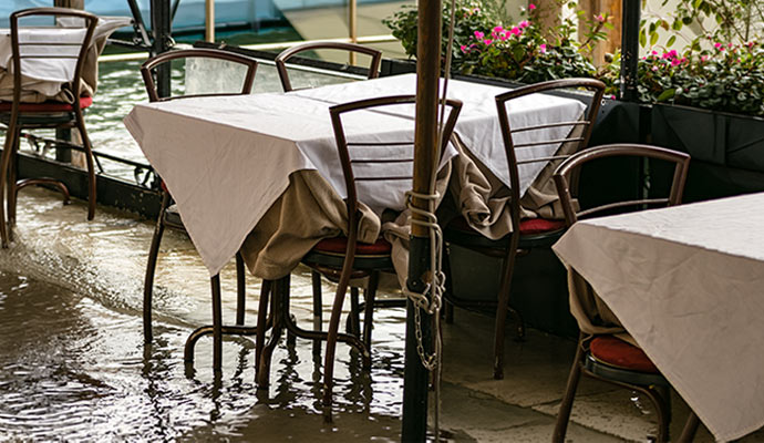 Restaurant patio flooded with standing water around dining tables and chairs after severe flood damage