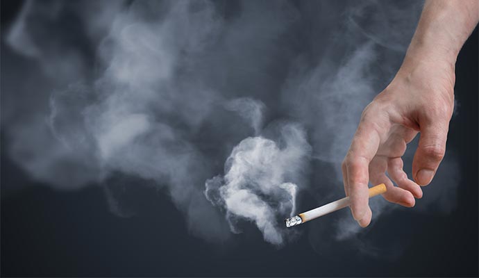 Close-up view of a hand holding a lit cigarette with smoke swirling around