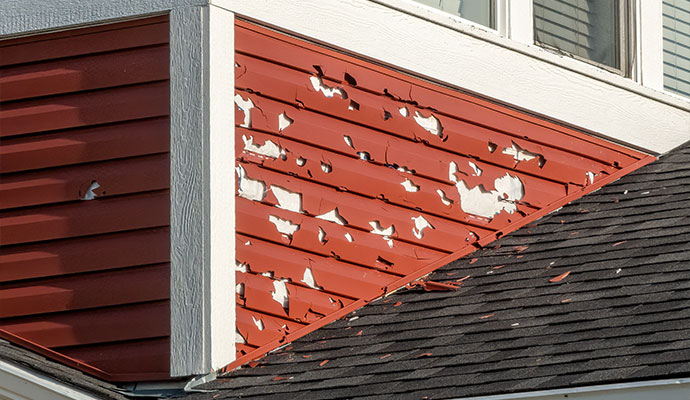 Cracked and broken red vinyl siding from hail damage