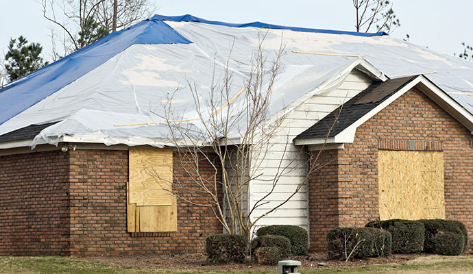 Damaged brick house secured with roof tarps and window boards