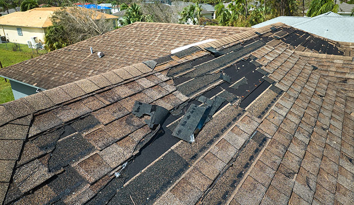 Torn roof shingles and exposed underlayment after storm damage