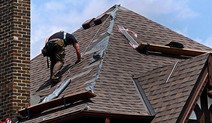 Expert repairing steep shingle roof near brick chimney An expert repairing a steep shingle roof using tools and a safety harness near a brick chimney
