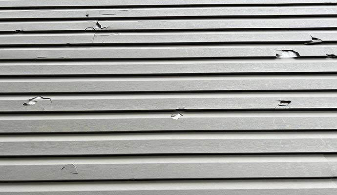 Hail-damaged vinyl siding with visible cracks
