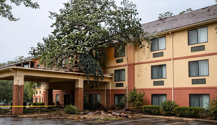 Hotel building with severe storm damage fallen tree debris and structural impact after extreme weather event