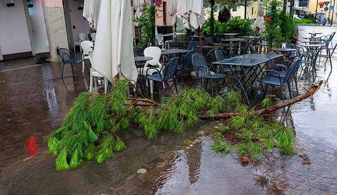Outdoor restaurant patio flooded with storm water debris and fallen tree branch after severe weather damage