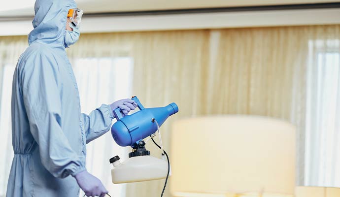 Technician in protective suit holding a disinfectant fogger machine