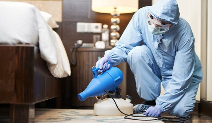 Technician sanitizing a bedroom with a disinfectant fogger machine